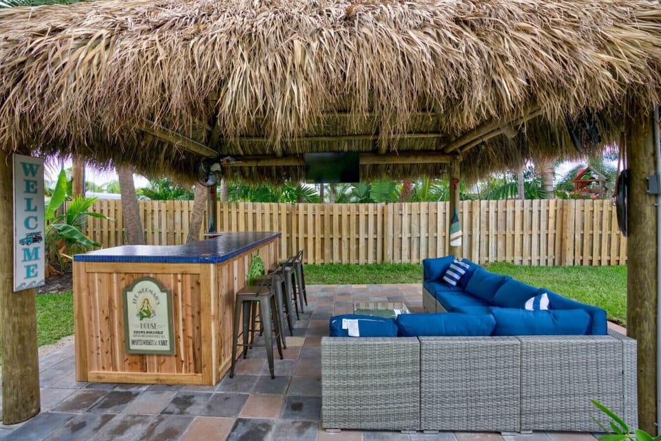 Relax under the tropical tiki hut featuring a custom bar, comfortable seating, and backyard views.