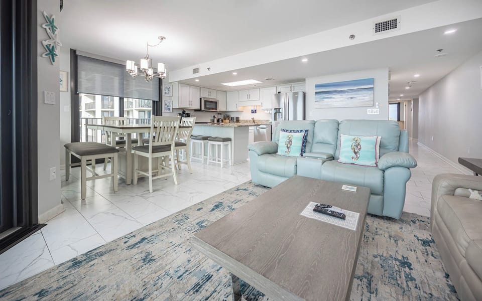 Bright living area features a cozy blue sofa with queen sleeper, a dining table, and a kitchen with granite countertops