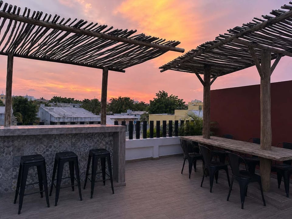 Sunset glowing over the rooftop lounge, high stools and a wood pergola for laid-back evenings