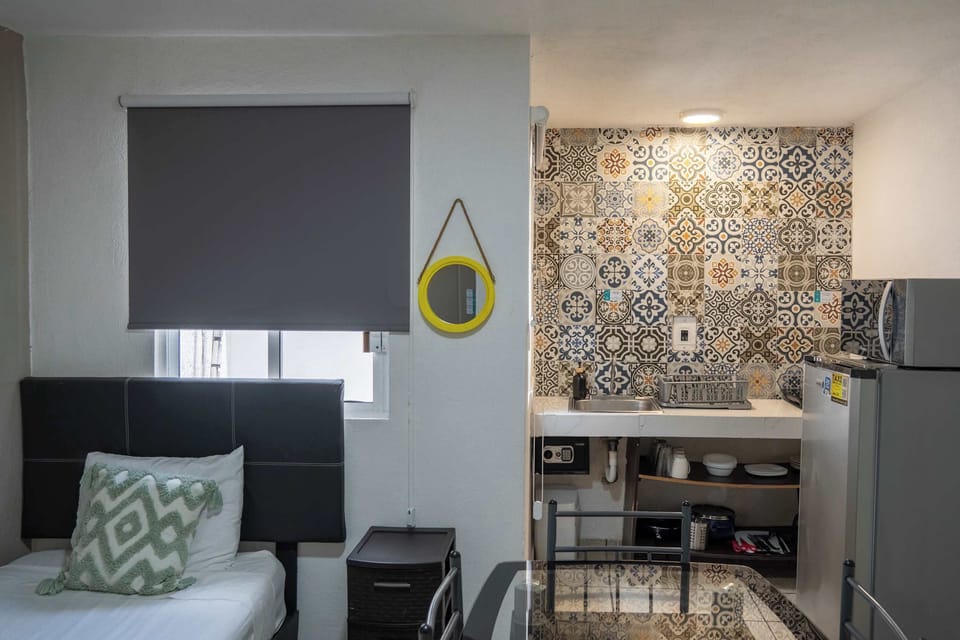 Smart studio pairing a cozy bed with a compact kitchen and vibrant tile, everything within reach
