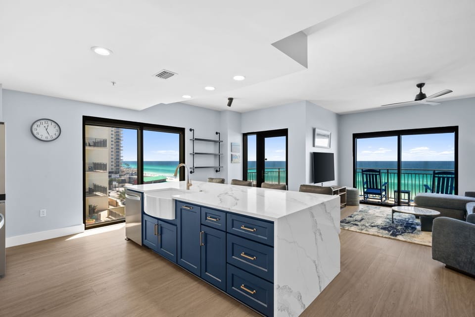 Your stunning oceanfront kitchen flows seamlessly into the living area, where turquoise waters stretch endlessly beyond floor-to-ceiling windows.