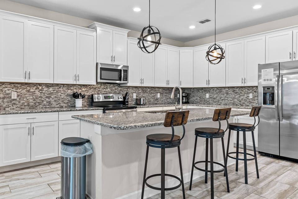 Welcome to this contemporary kitchen featuring sleek white cabinetry and a textured backsplash. The spacious island with stylish bar stools is perfect for casual dining, while modern pendant lights create a warm atmosphere.