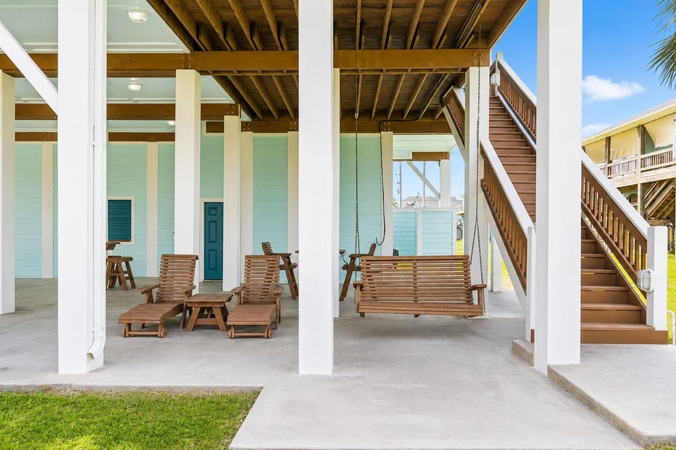 Covered ground-level entertainment area with seating, a porch swing, bar-height stools, lighting, and direct access to the yard.