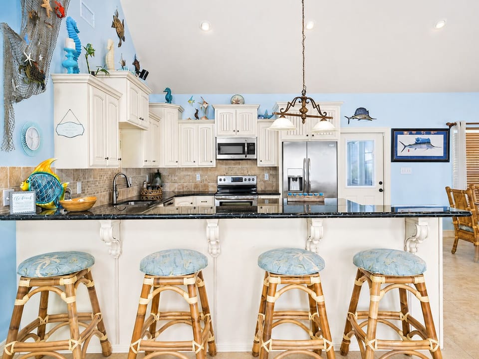 Kitchen breakfast bar with four stools, granite countertops, pendant lighting, white cabinetry, and stainless steel appliances.