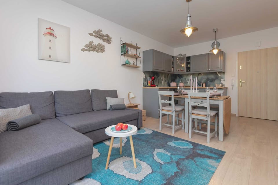 A modern living room featuring a gray sofa, a glass coffee table, and colorful artwork. The space is filled with natural light coming from large windows.
