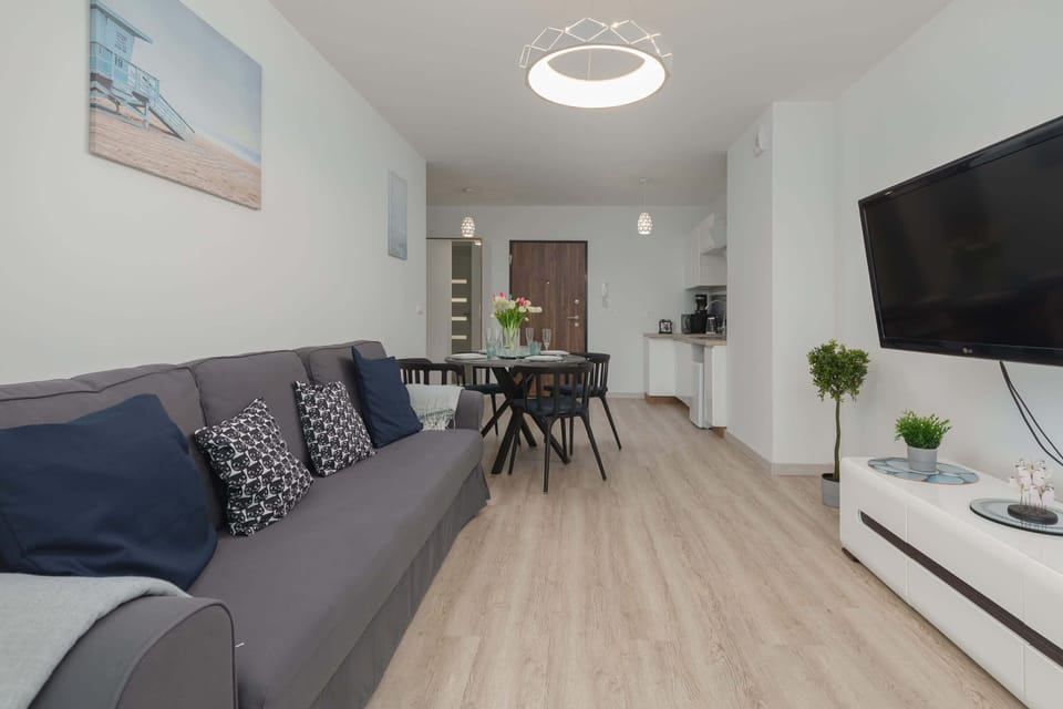 A spacious living room with a large gray sofa and a TV mounted on the wall. Light wood floors add to the modern look.