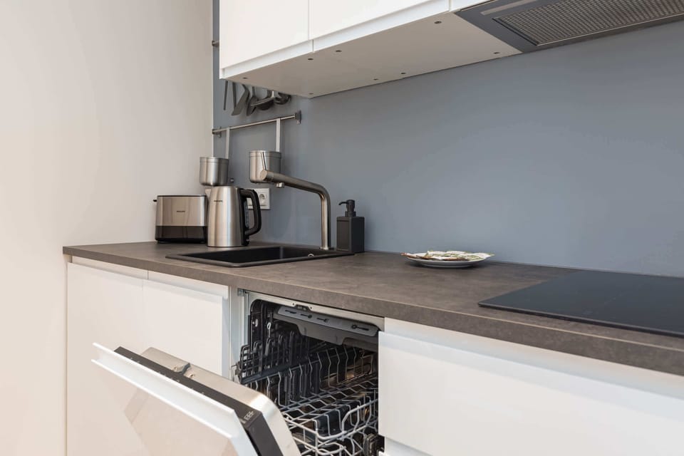 A modern kitchen with a long countertop, sleek appliances, and a view of the living area.