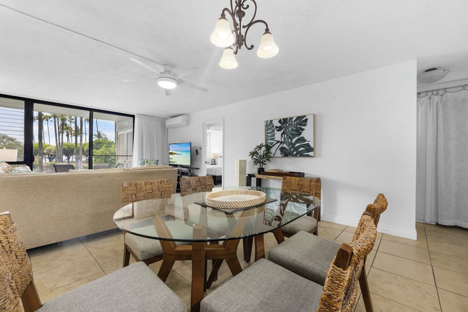 Gather around the handsome glass dining table and enjoy fresh coastal breezes from your private balcony, framed by swaying palms and warm natural light.
