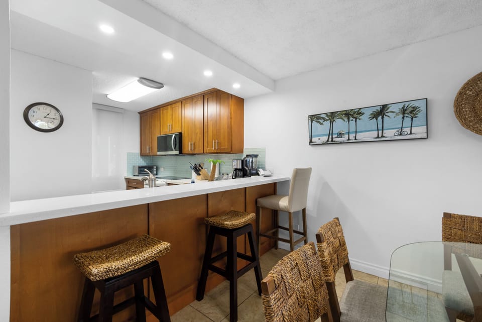 Your spacious kitchen features warm wood cabinetry, gleaming white countertops, and modern appliances—perfect for preparing meals during your stay. Enjoy coffee at the breakfast bar or gather around the dining table.