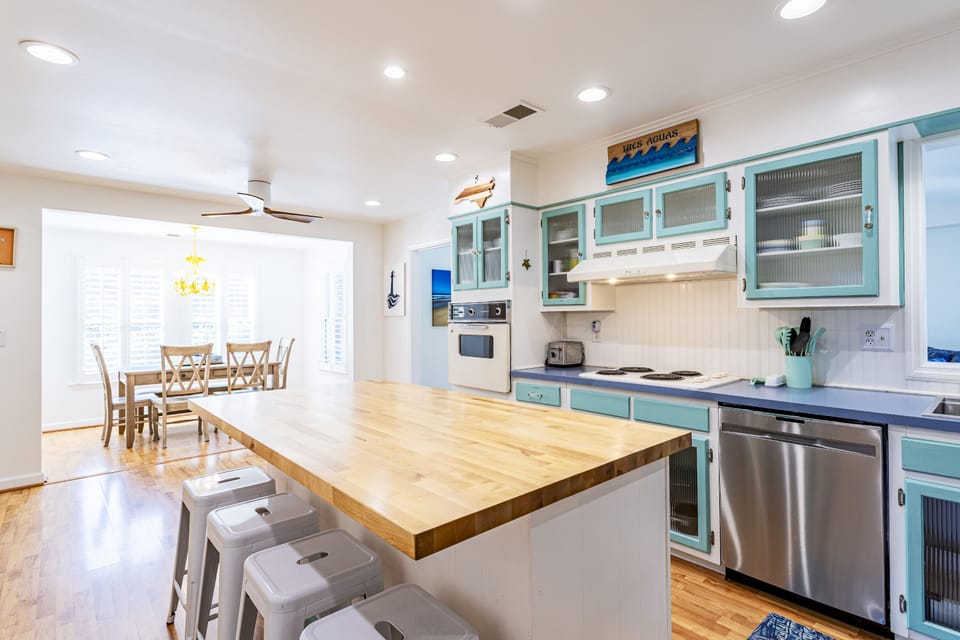Kitchen includes four bar stools by the island, oven, toaster, range, and plenty of tongs, spatulas, cookware, and pans.