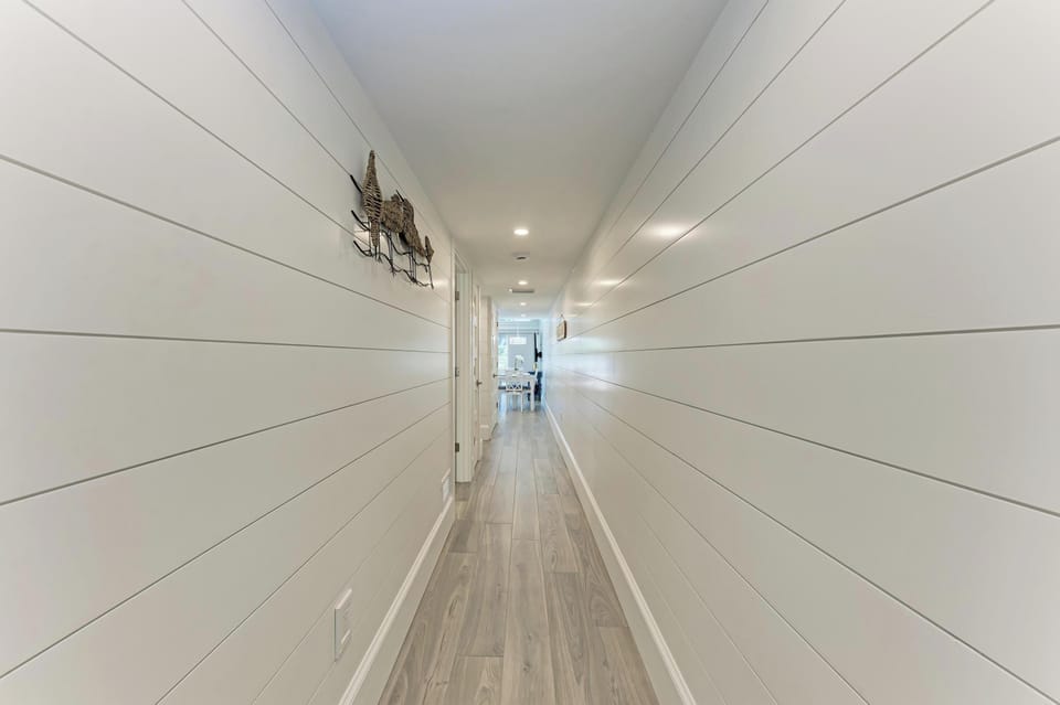 Walk through this bright hallway with crisp white shiplap walls and gleaming hardwood floors that lead to your spacious living areas ahead.