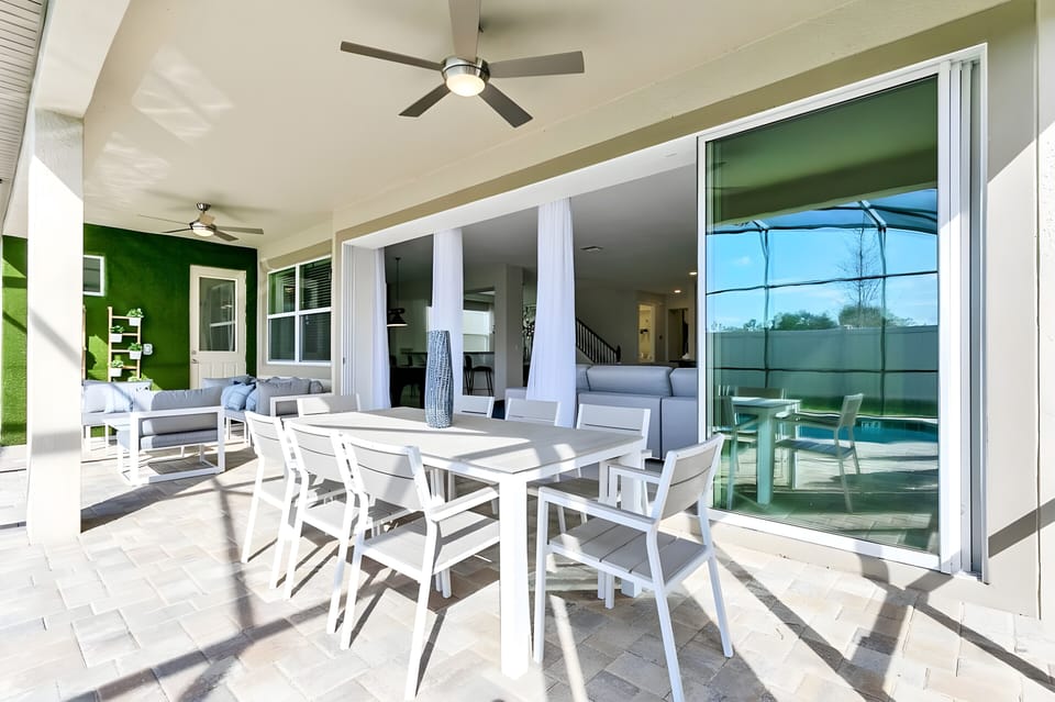 Enjoy al fresco dining in our spacious outdoor area, featuring a sleek white table and comfy chairs. Large sliding glass doors let in natural light and showcase lush green walls, creating a refreshing and inviting atmosphere.
