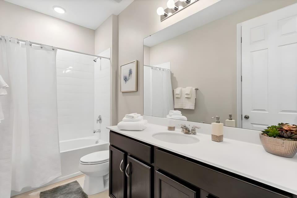 Experience a bright and airy bathroom with a stylish double vanity and rich dark cabinetry that beautifully contrasts the light walls. Enjoy the spaciousness, plush towels, and calming decor for a relaxing retreat.