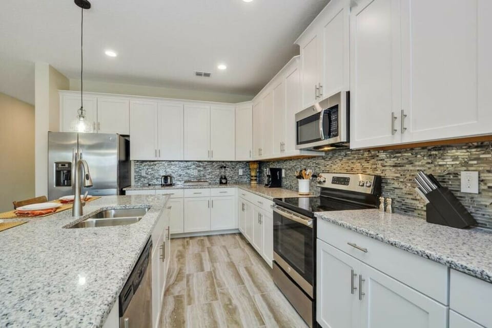 Enjoy a stunning kitchen with elegant white cabinetry, gleaming granite countertops, and modern stainless steel appliances. The subtle mosaic backsplash enhances the inviting space, ideal for cooking and connecting with friends.