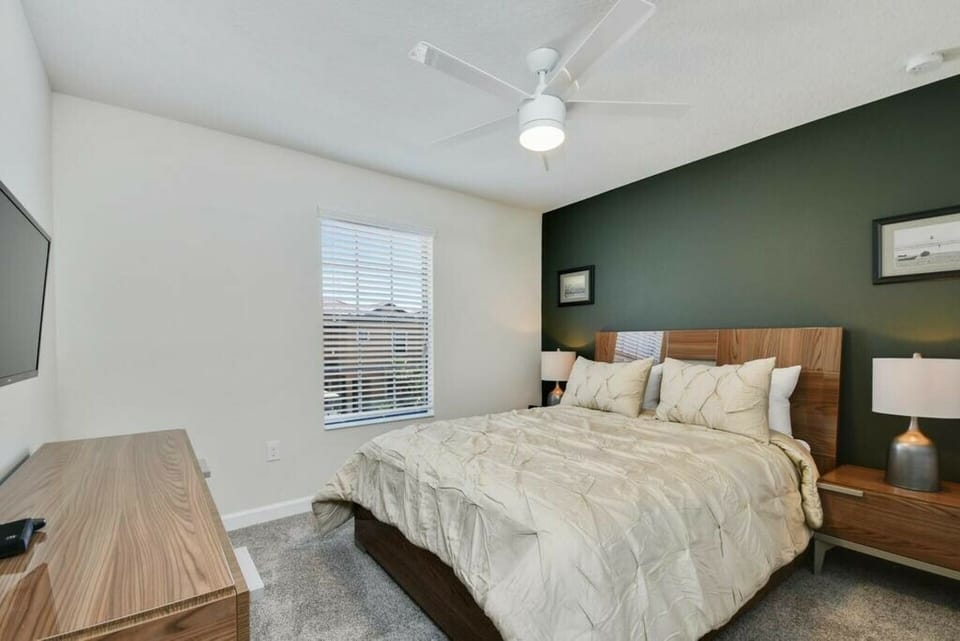 Unwind in this inviting bedroom with a rich green accent wall and a cozy wooden bed. Soft bedding and chic lamps create a warm atmosphere, while natural light from the window adds to your relaxing experience.