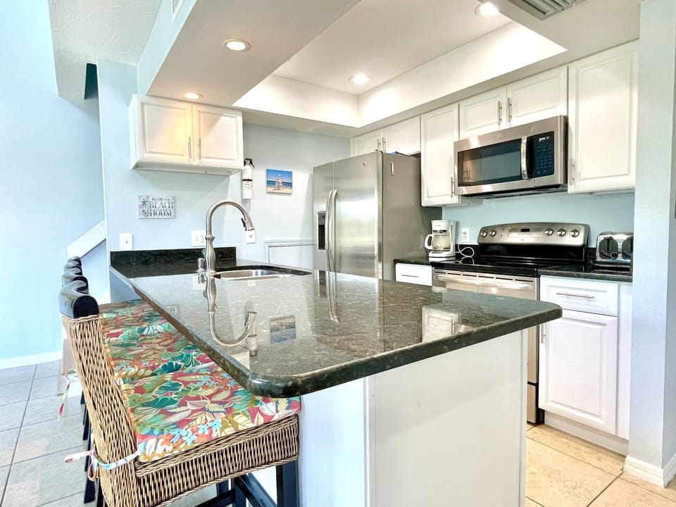 Kitchen with dark granite island, white cabinets, stainless steel microwave, refrigerator, and tropical table runner accent