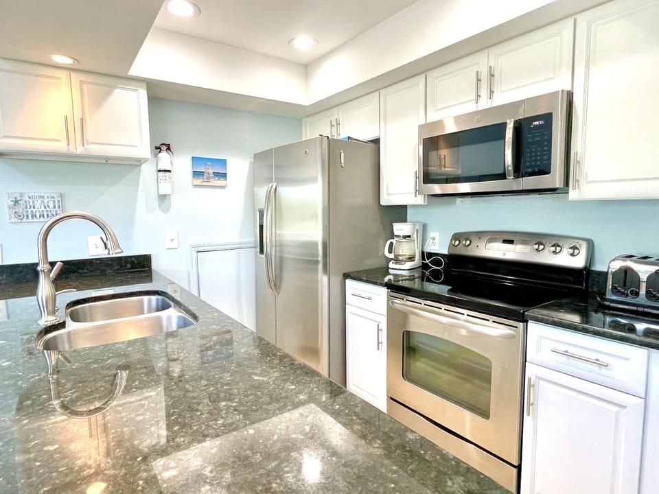 Kitchen with white cabinets, stainless steel microwave and refrigerator, electric range, and granite countertop with sink