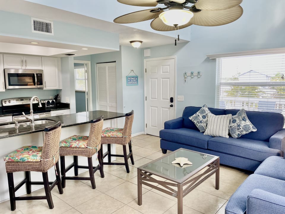 Open-plan kitchen and living area with dark granite island, bar stools, and sofa visible in background