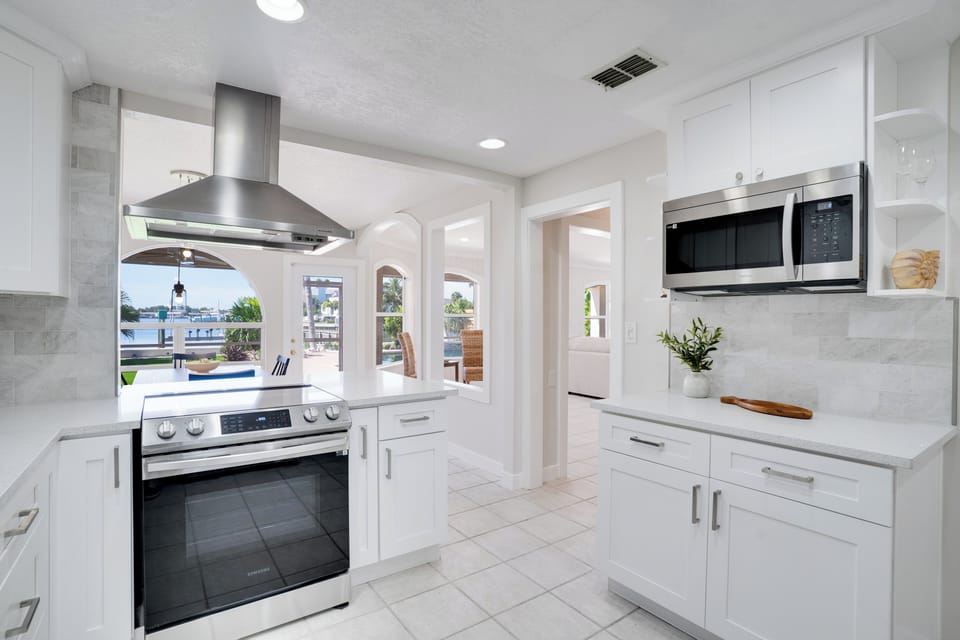 Your pristine white kitchen features modern appliances and marble countertops, perfect for preparing meals while enjoying views through bright windows.