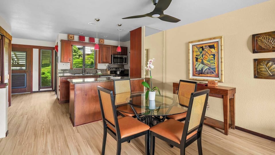 Gather around this elegant dining space where tropical artwork and warm wood tones create a welcoming island ambiance. Your fully equipped kitchen invites easy meal prep while you enjoy views of lush greenery beyond.