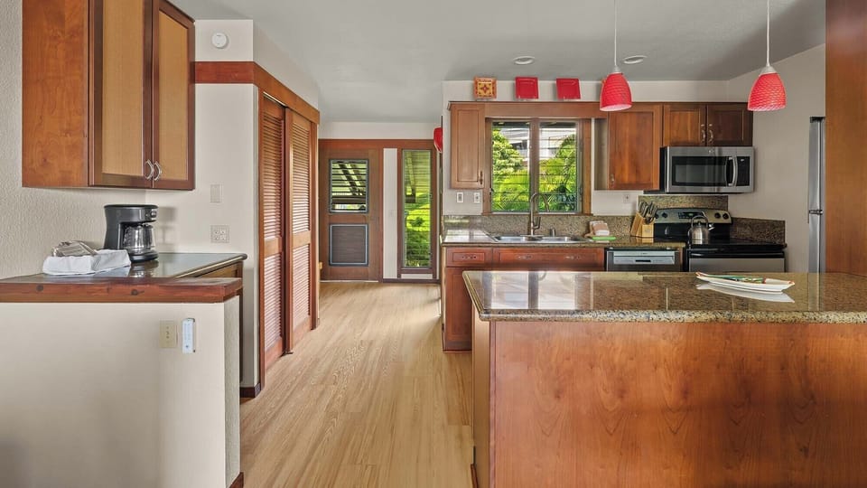 Step into your spacious open kitchen with warm wood cabinetry, granite counters, and a welcoming island perfect for prepping meals or savoring morning coffee while tropical breezes drift through the windows.