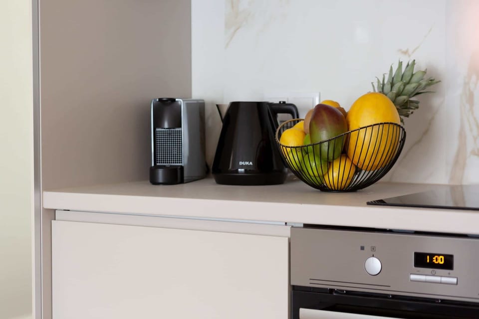 A close-up of a kitchen countertop featuring a black coffee maker, an electric kettle, and a colorful bowl of fruit, emphasizing the cozy and practical kitchen setting.