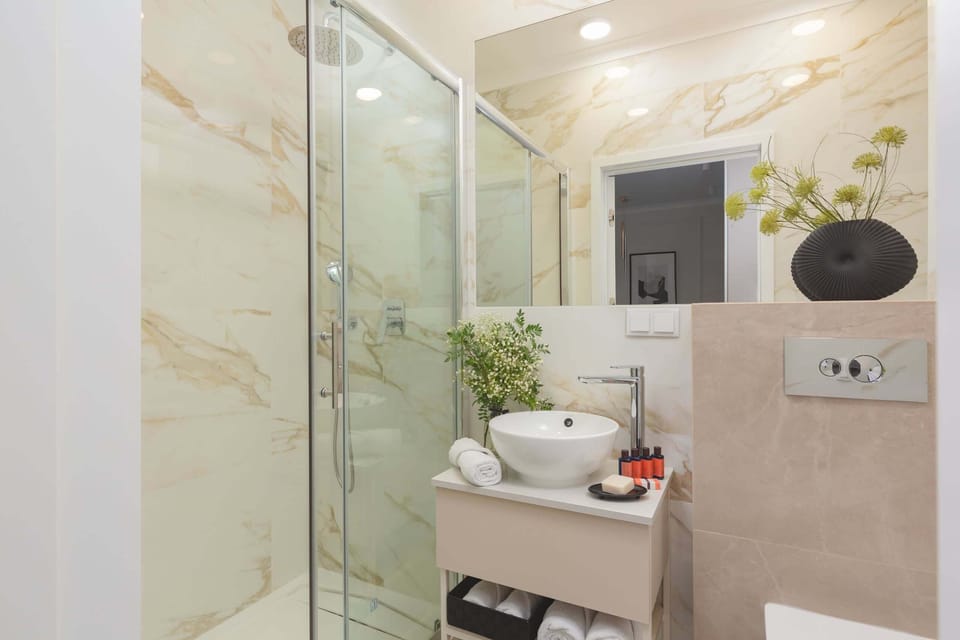 A bathroom with a modern, minimalistic design featuring a shower cabin with glass doors, white walls, and elegant fixtures.