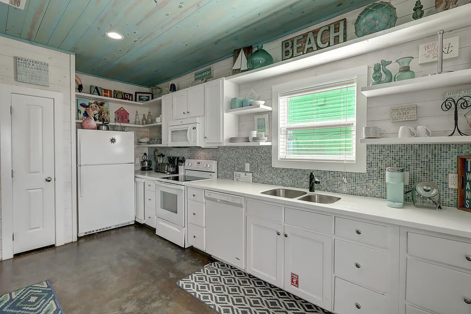 Your charming beach-themed kitchen features white cabinets, mosaic tile backsplash, and coastal decor creating a relaxing cooking space.