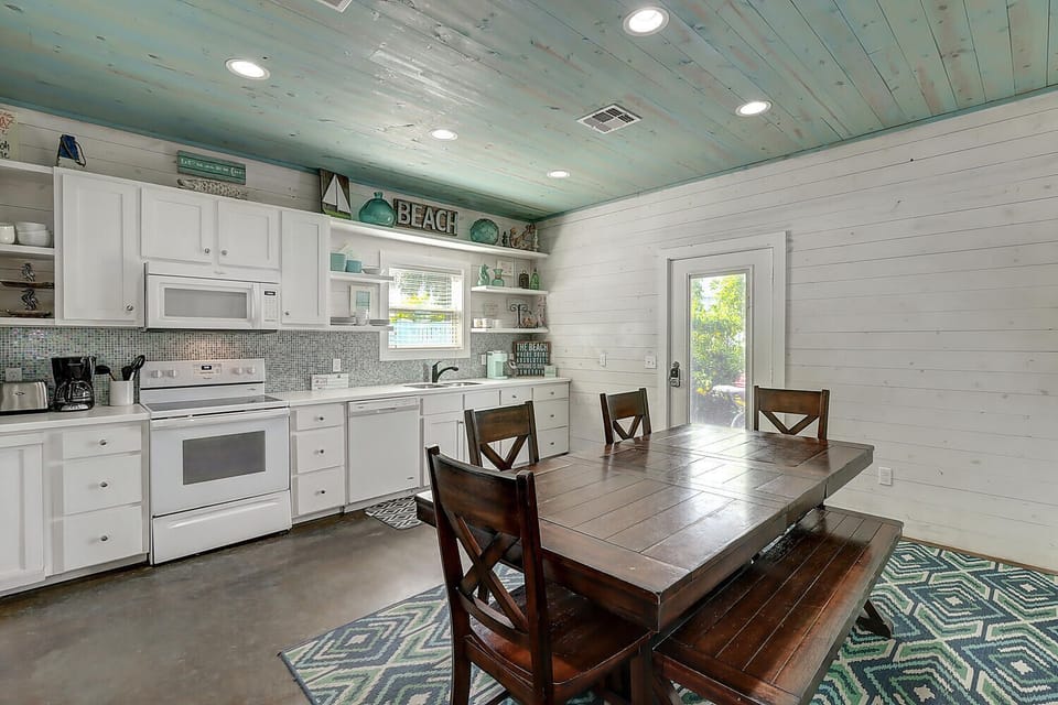 Gather around your coastal-inspired dining table in this bright kitchen where beach vibes meet home comfort through charming shiplap walls.