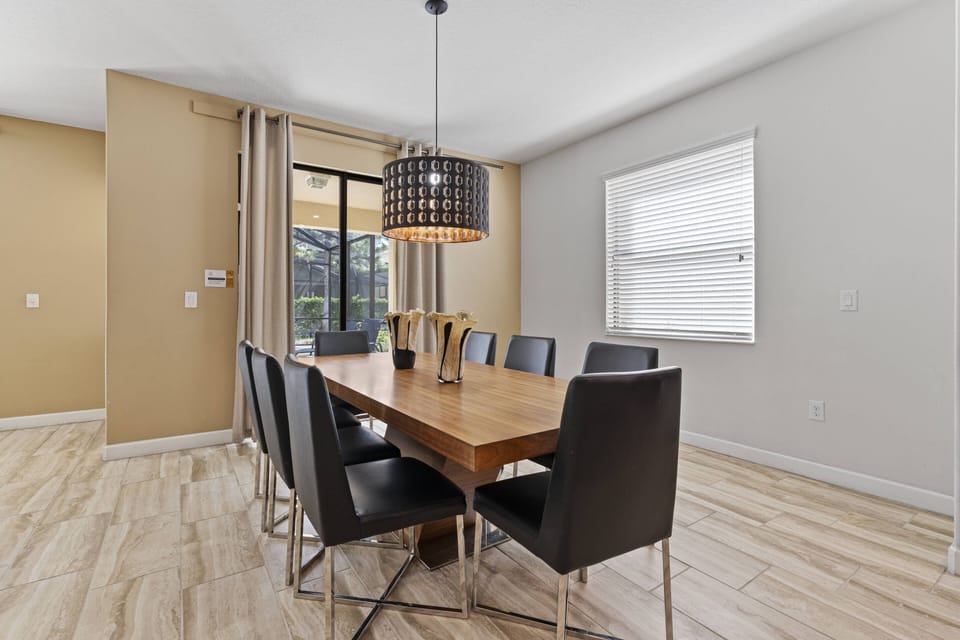 This bright dining area boasts a sleek wooden table with modern black chairs, ideal for family meals. A stylish pendant light adds sophistication, while large windows invite natural light, creating a warm and welcoming atmosphere.