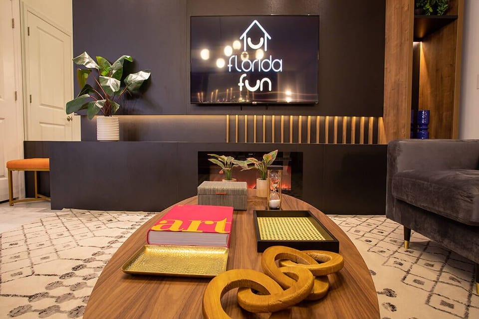 Enjoy laid-back gatherings in this stylish living area, where a sleek wooden coffee table holds vibrant books and unique decor. The warm tones of the plush sofa complement the modern wall-mounted TV for a cozy vibe.