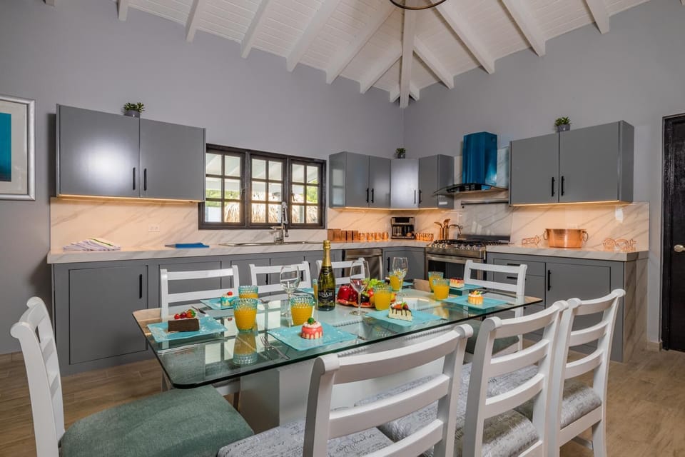 This dining and kitchen area has an elegant color interior.  There is plenty of storage space in the full kitchen. There is an 8-seater table and cushioned chairs in the dining area.