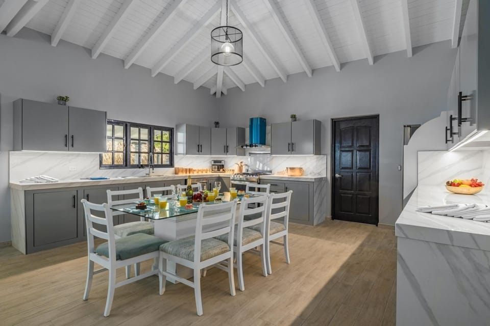 This dining and kitchen area has an elegant color interior.  There is plenty of storage space in the full kitchen. There is an 8-seater table and cushioned chairs in the dining area.