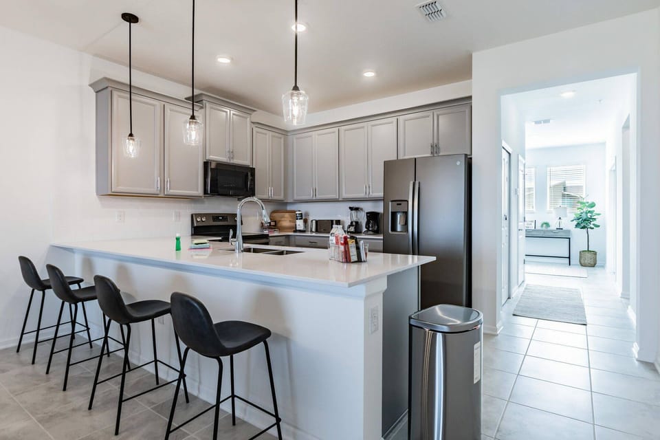 This contemporary kitchen features sleek gray cabinetry and a spacious island, perfect for casual meals or morning coffee. The pendant lighting adds a warm glow, while the open layout seamlessly connects to the inviting entryway.