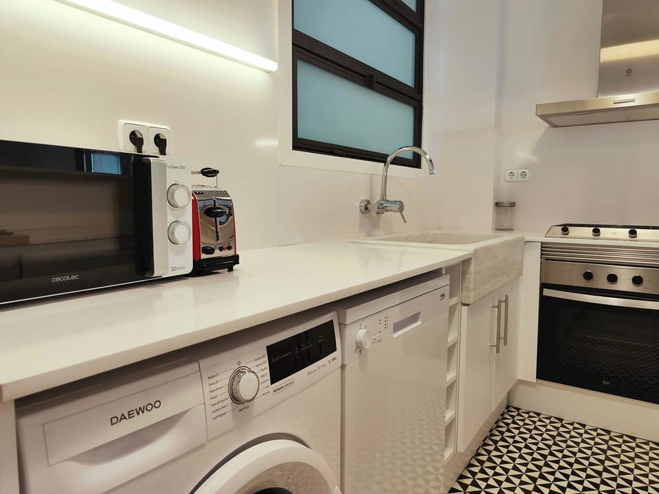 The apartment's kitchen features a modern design with sleek white cabinets, a stainless steel range hood, and a white countertop. The kitchen is fully equipped with a refrigerator, washing machine, dishwasher, oven, microwave, toaster, and other appliance