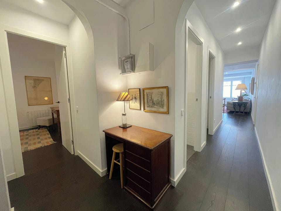 The hallway of this apartment is a bright and airy space, featuring white walls and dark wood floors. The hallway offers access to other rooms, which can be glimpsed through the open doorways. This space provides a welcoming entryway to this charming apar