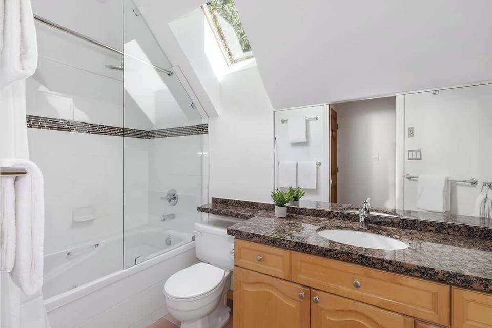 - Bright bathroom with skylight and spacious glass shower tub  
- Granite countertop, large mirror, and soft white towels included  
- Modern design creates a refreshing start and end to your day  
