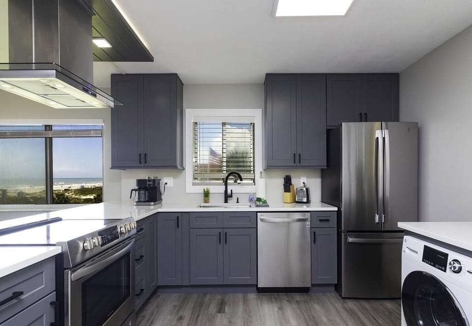 Gray shaker cabinets and white quartz countertops surround stainless steel appliances and a black faucet in the kitchen.