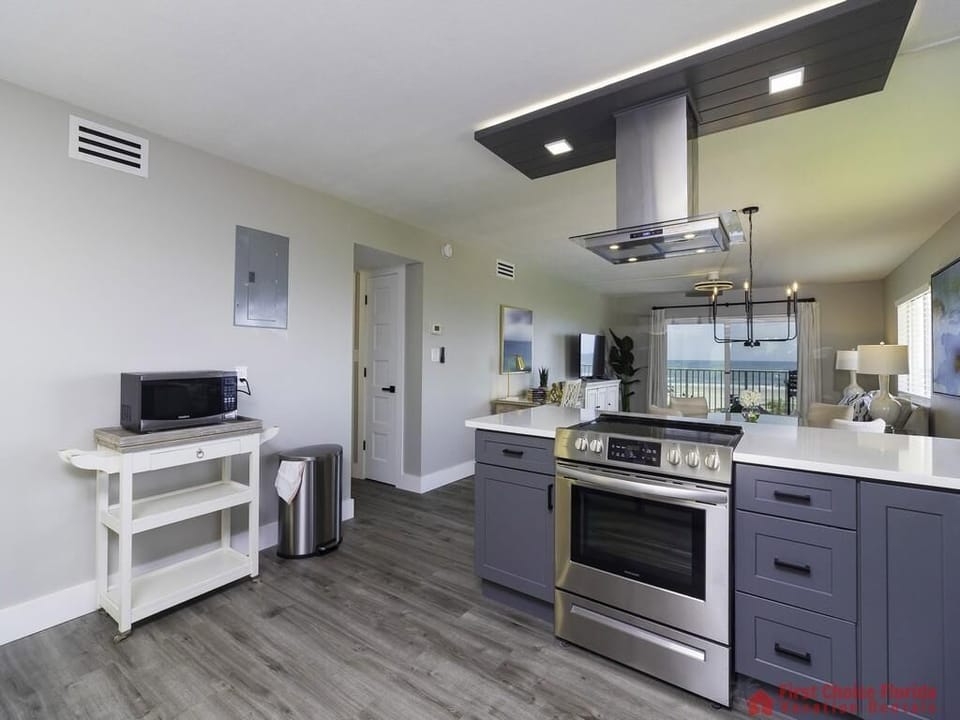 Blue shaker cabinets and white quartz countertops frame the stainless steel range beneath a modern vent hood in the kitchen.