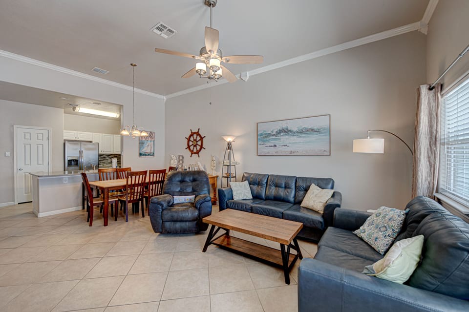 Relax in your spacious open-concept living area featuring plush leather seating, coastal décor, and a fully equipped kitchen perfect for family gatherings.