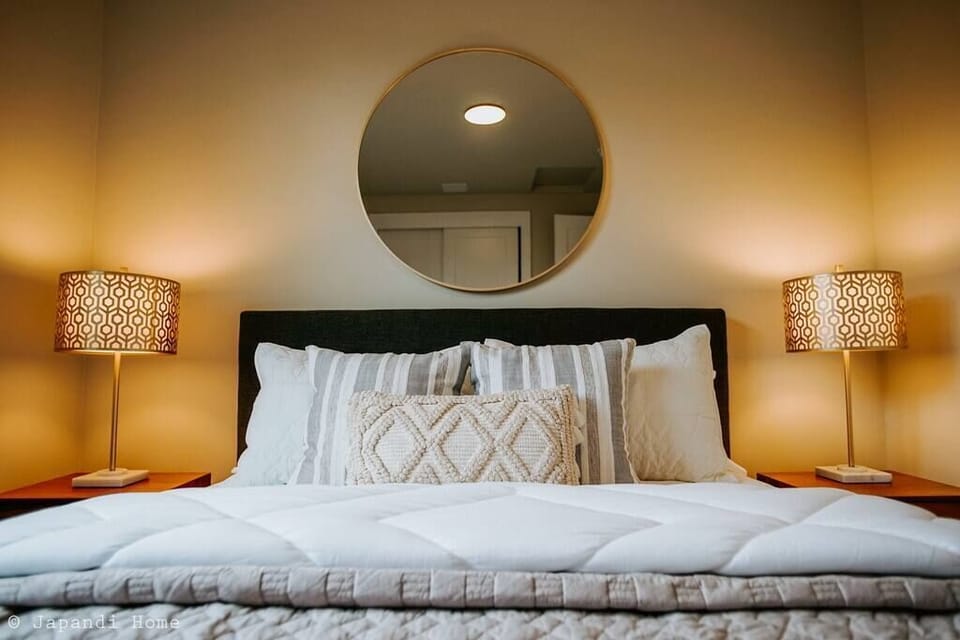 Golden circular mirror over the cozy bed frame brings a classy accent to the room