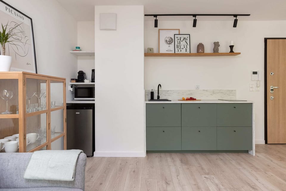 A modern kitchen with a simple design, featuring light green cabinetry and open shelving, giving it a clean and uncluttered appearance.