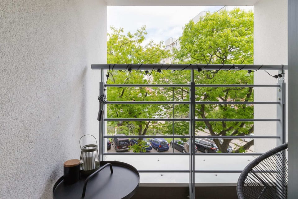 A compact balcony with a simple table and chair set, surrounded by greenery, making it a perfect spot for outdoor relaxation.