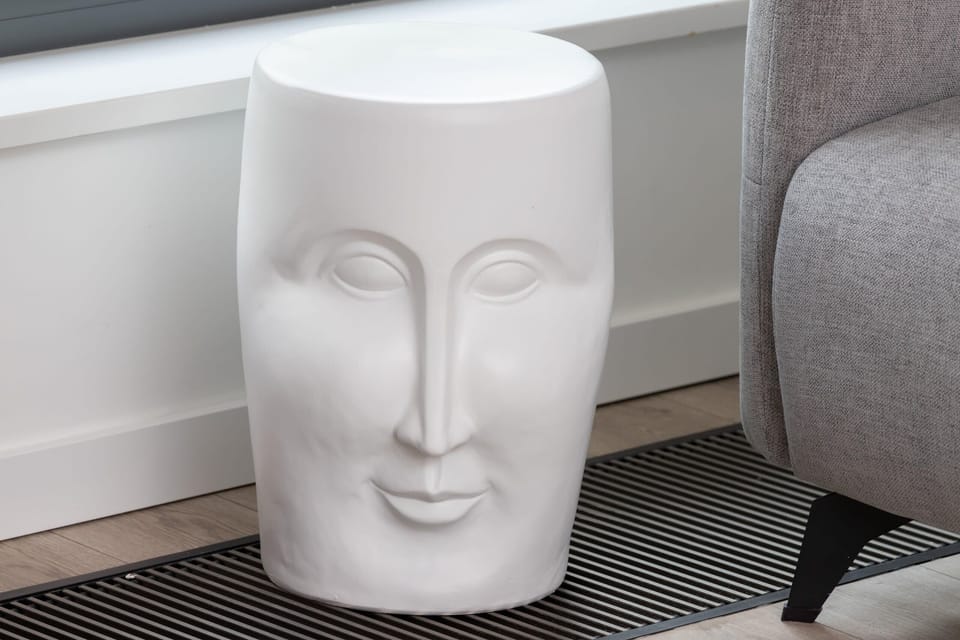 An artistic white sculpture of a head, placed next to a comfortable gray armchair, adding a unique and modern decorative element.
