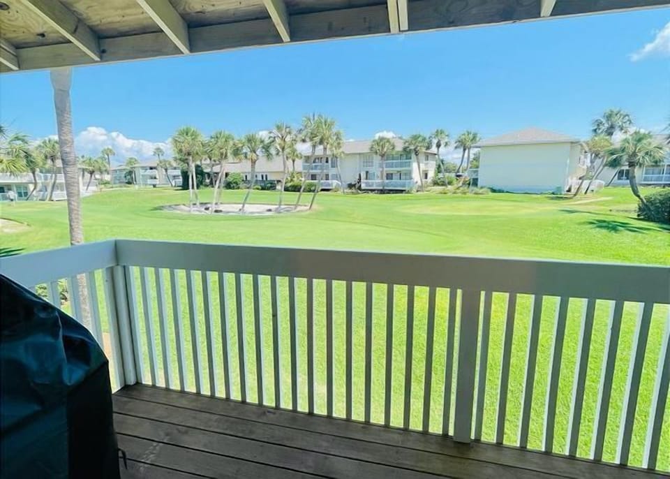 Your covered balcony overlooks lush green lawns and palm trees, creating a peaceful tropical retreat perfect for morning coffee or evening relaxation.