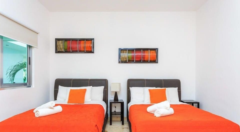 Bright bedroom with two queen beds featuring vibrant orange bedding and modern decor.