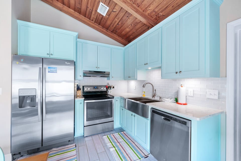 Your fully equipped kitchen features charming turquoise cabinets and stainless steel appliances, perfect for preparing meals in this coastal-inspired space.