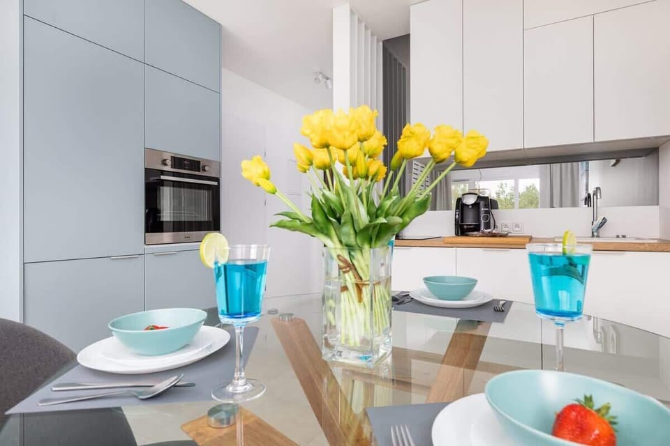 A kitchen area with white cabinets and a countertop equipped with essentials, including a coffee machine and glassware. The design is modern and efficient.