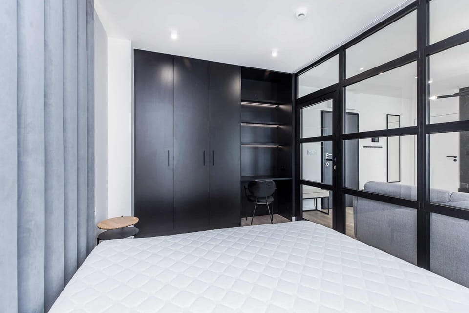 A minimalist bedroom with a large bed, soft neutral bedding, and ample natural light coming through large windows, creating a serene and peaceful space.