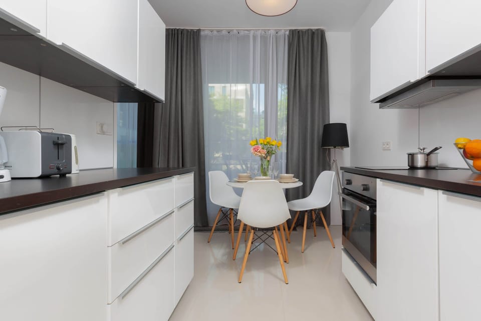 Fully equipped modern kitchen with white cabinetry, dark countertops, and bright natural light.
